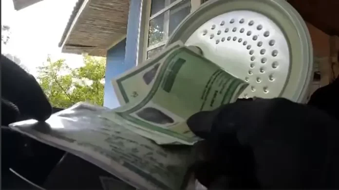 Mãos de policial federal segurando documentos apreendidos durante operação que investiga fraude bancária.