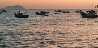 Vários barcos de pesca no mar ao nascer do sol, indicando tempo firme e ensolarado.