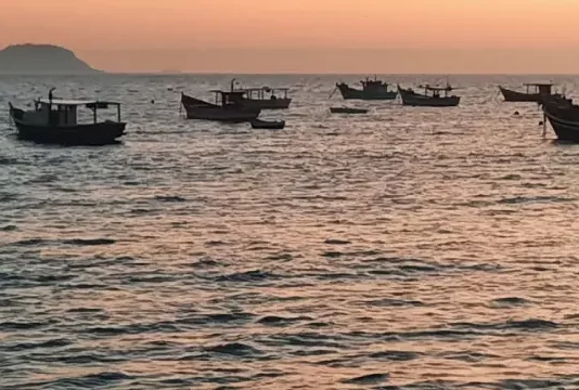 Vários barcos de pesca no mar ao nascer do sol, indicando tempo firme e ensolarado.