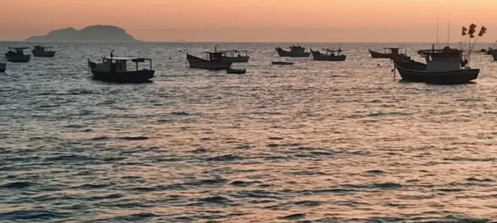 Vários barcos de pesca no mar ao nascer do sol, indicando tempo firme e ensolarado.