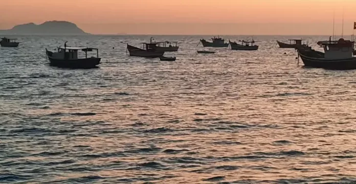 Vários barcos de pesca no mar ao nascer do sol, indicando tempo firme e ensolarado.