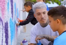 Rhuan Santo orienta uma criança sobre técnicas de grafite em parede, simbolizando a integração entre arte urbana e educação.