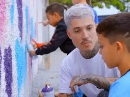 Rhuan Santo orienta uma criança sobre técnicas de grafite em parede, simbolizando a integração entre arte urbana e educação.