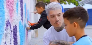Rhuan Santo orienta uma criança sobre técnicas de grafite em parede, simbolizando a integração entre arte urbana e educação.