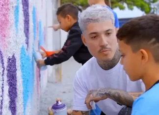 Rhuan Santo orienta uma criança sobre técnicas de grafite em parede, simbolizando a integração entre arte urbana e educação.