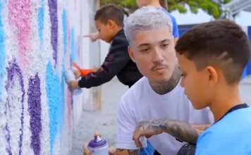 Rhuan Santo orienta uma criança sobre técnicas de grafite em parede, simbolizando a integração entre arte urbana e educação.