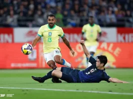 Jogador da seleção brasileira tenta avançar com a bola enquanto é desarmado por um defensor da seleção japonesa durante uma partida de futebol. A imagem ilustra o confronto entre Brasil e Japão, usada para representar o tema do desempenho da seleção brasileira.