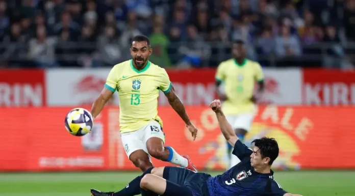 Jogador da seleção brasileira tenta avançar com a bola enquanto é desarmado por um defensor da seleção japonesa durante uma partida de futebol. A imagem ilustra o confronto entre Brasil e Japão, usada para representar o tema do desempenho da seleção brasileira.