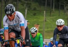 Grupo de ciclistas participa de uma competição em estrada durante o dia. Os atletas usam uniformes e capacetes de segurança, pedalando em alta velocidade. A imagem representa o contexto esportivo da Volta Ciclística de Santa Catarina, com foco no esforço físico dos competidores e no dinamismo da prova. Ao fundo, é possível ver uma área verde com árvores, sugerindo um percurso em meio à natureza.