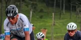 Grupo de ciclistas participa de uma competição em estrada durante o dia. Os atletas usam uniformes e capacetes de segurança, pedalando em alta velocidade. A imagem representa o contexto esportivo da Volta Ciclística de Santa Catarina, com foco no esforço físico dos competidores e no dinamismo da prova. Ao fundo, é possível ver uma área verde com árvores, sugerindo um percurso em meio à natureza.