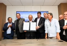 Foto dos líderes políticos de São José e de Santa Catarina durante o lançamento dos editais de construção da Beira-Mar de Barreiros, segurando a pasta oficial que marca o início da obra.