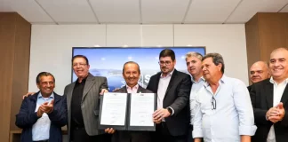 Foto dos líderes políticos de São José e de Santa Catarina durante o lançamento dos editais de construção da Beira-Mar de Barreiros, segurando a pasta oficial que marca o início da obra.