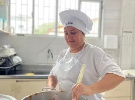 Maise Ferreira de Jesus, cozinheira da rede municipal de Florianópolis, prepara uma refeição em panela sobre o fogão, ilustrando seu trabalho na alimentação escolar