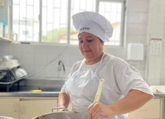 Maise Ferreira de Jesus, cozinheira da rede municipal de Florianópolis, prepara uma refeição em panela sobre o fogão, ilustrando seu trabalho na alimentação escolar