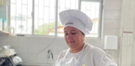 Maise Ferreira de Jesus, cozinheira da rede municipal de Florianópolis, prepara uma refeição em panela sobre o fogão, ilustrando seu trabalho na alimentação escolar