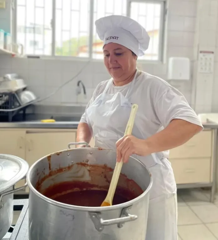 Maise Ferreira de Jesus, cozinheira da rede municipal de Florianópolis, prepara uma refeição em panela sobre o fogão, ilustrando seu trabalho na alimentação escolar
