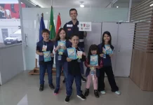 Crianças posam com o supervisor Silvio Dias, da Regional do Imetro de Tubarão, segurando cartilhas do Projeto Fiscal Mirim, destacando a iniciativa de ensino sobre fiscalização e metrologia.