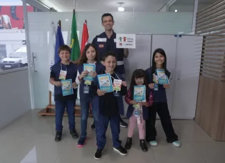 Crianças posam com o supervisor Silvio Dias, da Regional do Imetro de Tubarão, segurando cartilhas do Projeto Fiscal Mirim, destacando a iniciativa de ensino sobre fiscalização e metrologia.