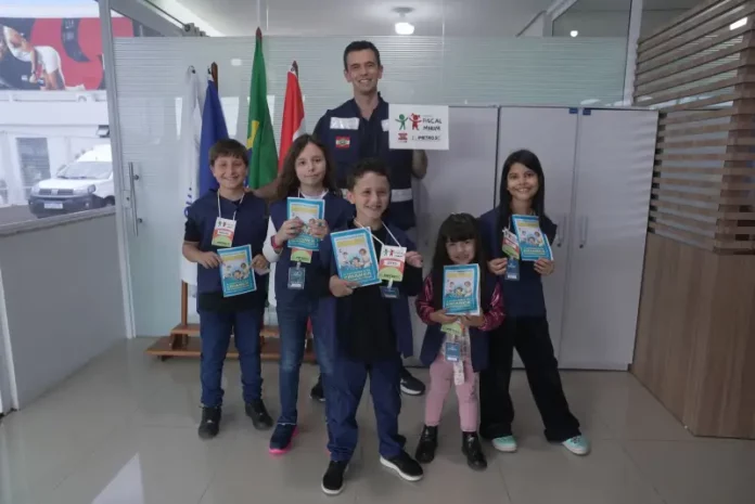 Crianças posam com o supervisor Silvio Dias, da Regional do Imetro de Tubarão, segurando cartilhas do Projeto Fiscal Mirim, destacando a iniciativa de ensino sobre fiscalização e metrologia.