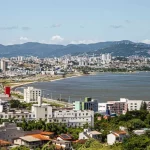 Perfil da população de São José: IBGE mostra cidade urbana e alfabetizada Vista aérea de São José mostrando o mar e a Beira-Mar, com prédios da cidade que ilustram o perfil urbano e populacional do município.