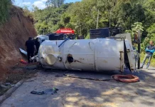 Caminhão capotado enquanto equipe de bombeiros realiza resgate do motorista preso nas ferragens.