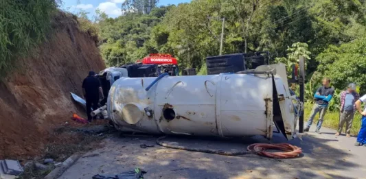 Caminhão capotado enquanto equipe de bombeiros realiza resgate do motorista preso nas ferragens.
