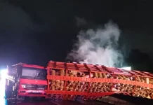 Acidente com caminhão carregado de botijões de gás tombado no vão central da pista em chamas, com outro caminhão colidido na traseira do veículo tombado.