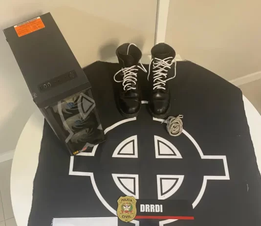 Polícia Civil apreende símbolos de apologia ao nazismo com adolescente de Palhoça Imagem mostra objetos apreendidos pela Polícia Civil durante o cumprimento de mandado, incluindo símbolos nazistas e equipamentos eletrônicos usados para divulgação de conteúdo racista.