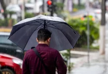 Frente fria mantém chuva intensa e temporais isolados em Santa Catarina Homem caminhando na chuva com guarda-chuva, mostrando os efeitos da frente fria que provoca chuva intensa e temporais isolados em Santa Catarina.
