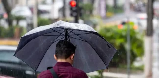 Homem caminhando na chuva com guarda-chuva, mostrando os efeitos da frente fria que provoca chuva intensa e temporais isolados em Santa Catarina.