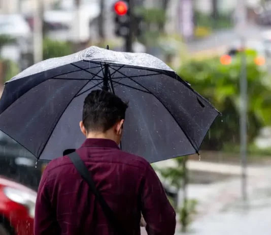 Homem caminhando na chuva com guarda-chuva, mostrando os efeitos da frente fria que provoca chuva intensa e temporais isolados em Santa Catarina.