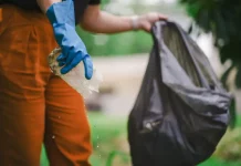 Homem recolhendo um pedaço de plástico com água parada para eliminar possíveis criadouros do mosquito Aedes aegypti e focos de dengue.