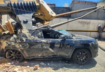 Imagem registrada para documentar os danos causados por um deslizamento de terra ocorrido na manhã de terça-feira, 14 de outubro, no Centro de Florianópolis. A foto mostra uma escavadeira tombada sobre um SUV preto estacionado, com danos significativos na estrutura do veículo. A máquina teria provocado o deslizamento ao operar em um terreno instável. A imagem tem como finalidade ilustrar os efeitos do acidente, demonstrando a gravidade da ocorrência e subsidiar ações de avaliação de risco, segurança e resposta das autoridades envolvidas, como o Corpo de Bombeiros e a Defesa Civil.