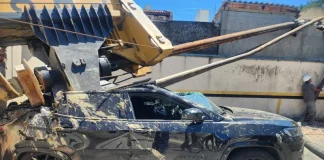 Imagem registrada para documentar os danos causados por um deslizamento de terra ocorrido na manhã de terça-feira, 14 de outubro, no Centro de Florianópolis. A foto mostra uma escavadeira tombada sobre um SUV preto estacionado, com danos significativos na estrutura do veículo. A máquina teria provocado o deslizamento ao operar em um terreno instável. A imagem tem como finalidade ilustrar os efeitos do acidente, demonstrando a gravidade da ocorrência e subsidiar ações de avaliação de risco, segurança e resposta das autoridades envolvidas, como o Corpo de Bombeiros e a Defesa Civil.