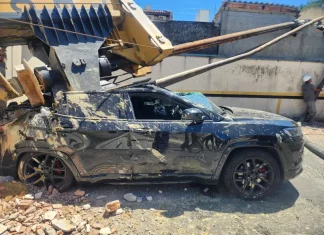 Imagem registrada para documentar os danos causados por um deslizamento de terra ocorrido na manhã de terça-feira, 14 de outubro, no Centro de Florianópolis. A foto mostra uma escavadeira tombada sobre um SUV preto estacionado, com danos significativos na estrutura do veículo. A máquina teria provocado o deslizamento ao operar em um terreno instável. A imagem tem como finalidade ilustrar os efeitos do acidente, demonstrando a gravidade da ocorrência e subsidiar ações de avaliação de risco, segurança e resposta das autoridades envolvidas, como o Corpo de Bombeiros e a Defesa Civil.