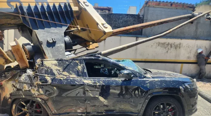 Imagem registrada para documentar os danos causados por um deslizamento de terra ocorrido na manhã de terça-feira, 14 de outubro, no Centro de Florianópolis. A foto mostra uma escavadeira tombada sobre um SUV preto estacionado, com danos significativos na estrutura do veículo. A máquina teria provocado o deslizamento ao operar em um terreno instável. A imagem tem como finalidade ilustrar os efeitos do acidente, demonstrando a gravidade da ocorrência e subsidiar ações de avaliação de risco, segurança e resposta das autoridades envolvidas, como o Corpo de Bombeiros e a Defesa Civil.