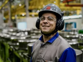 Santa Catarina mantém a menor taxa de desemprego do país, aponta Censo Operário sorrindo em linha de produção, usando capacete, óculos e uniforme, simbolizando o baixo desemprego em Santa Catarina, o menor do país segundo o Censo 2022.