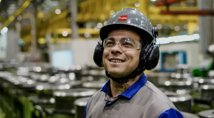 Santa Catarina mantém a menor taxa de desemprego do país, aponta Censo Operário sorrindo em linha de produção, usando capacete, óculos e uniforme, simbolizando o baixo desemprego em Santa Catarina, o menor do país segundo o Censo 2022.