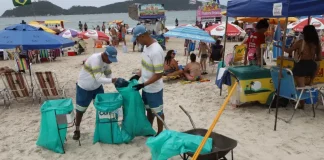 Garis coletando lixo na praia durante o verão, ilustrando a contratação temporária da Comcap.