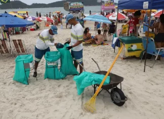 Florianópolis convoca 371 temporários para reforço na limpeza do verão Garis coletando lixo na praia durante o verão, ilustrando a contratação temporária da Comcap para reforço na limpeza