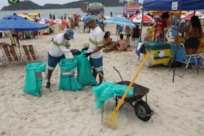 limpeza pública Garis coletando lixo na praia durante o verão, ilustrando a contratação temporária da Comcap.