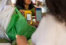 Cliente realiza pagamento por QR Code em maquininha de cartão durante compra em feira livre, representando o uso de tecnologia no comércio de micro e pequenas empresas.