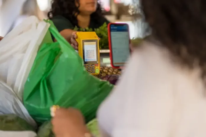 Cliente realiza pagamento por QR Code em maquininha de cartão durante compra em feira livre, representando o uso de tecnologia no comércio de micro e pequenas empresas.