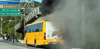 A imagem mostra um ônibus amarelo em chamas após a colisão com uma motocicleta. O registro evidencia a gravidade do acidente, que resultou na morte do motociclista, e a atuação das equipes de resgate diante do incêndio.