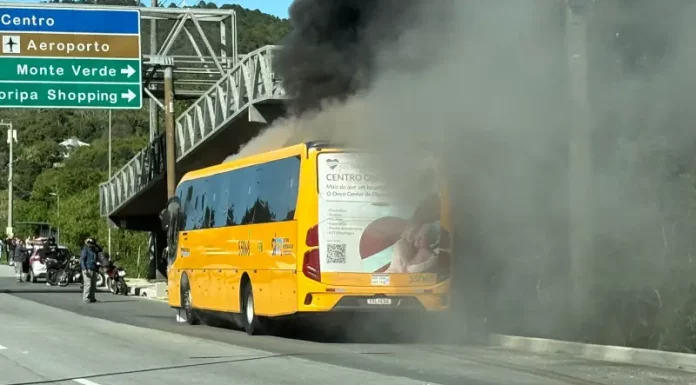 A imagem mostra um ônibus amarelo em chamas após a colisão com uma motocicleta. O registro evidencia a gravidade do acidente, que resultou na morte do motociclista, e a atuação das equipes de resgate diante do incêndio.