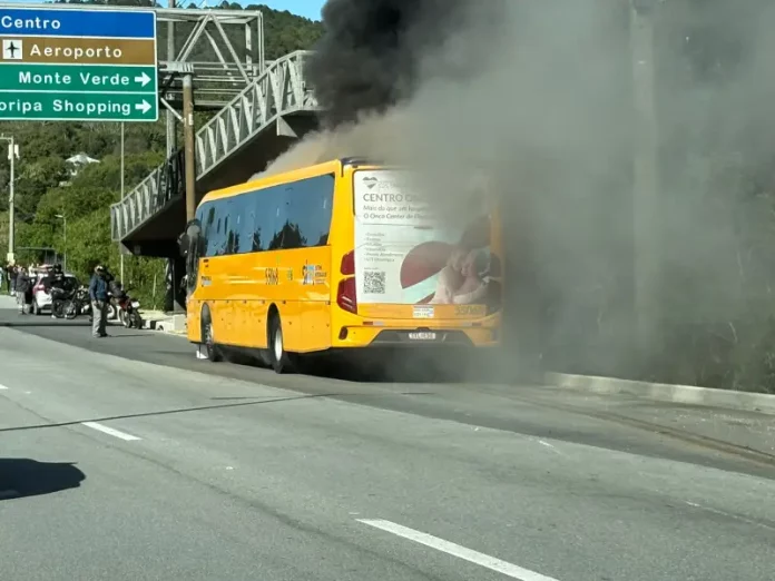 A imagem mostra um ônibus amarelo em chamas após a colisão com uma motocicleta. O registro evidencia a gravidade do acidente, que resultou na morte do motociclista, e a atuação das equipes de resgate diante do incêndio.