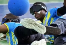 Dois atletas com deficiência visual disputam uma partida de goalball, esporte paralímpico. Ambos usam vendas nos olhos e uniformes esportivos. Um deles está em movimento defensivo, tentando bloquear uma bola azul com o corpo. A imagem representa o dinamismo e a inclusão no paradesporto, contexto do edital lançado pela Fesporte para apoiar projetos esportivos voltados a pessoas com deficiência em Santa Catarina.