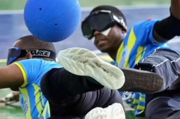 Dois atletas com deficiência visual disputam uma partida de goalball, esporte paralímpico. Ambos usam vendas nos olhos e uniformes esportivos. Um deles está em movimento defensivo, tentando bloquear uma bola azul com o corpo. A imagem representa o dinamismo e a inclusão no paradesporto, contexto do edital lançado pela Fesporte para apoiar projetos esportivos voltados a pessoas com deficiência em Santa Catarina.
