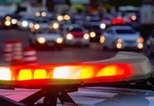 Luzes vermelhas e amarelas de uma viatura policial acesas em primeiro plano, com o trânsito urbano desfocado ao fundo, simbolizando a atuação das forças de segurança no combate aos homicídios e na redução da violência em Santa Catarina.