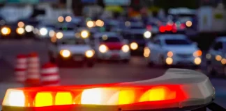 Luzes vermelhas e amarelas de uma viatura policial acesas em primeiro plano, com o trânsito urbano desfocado ao fundo, simbolizando a atuação das forças de segurança no combate aos homicídios e na redução da violência em Santa Catarina.